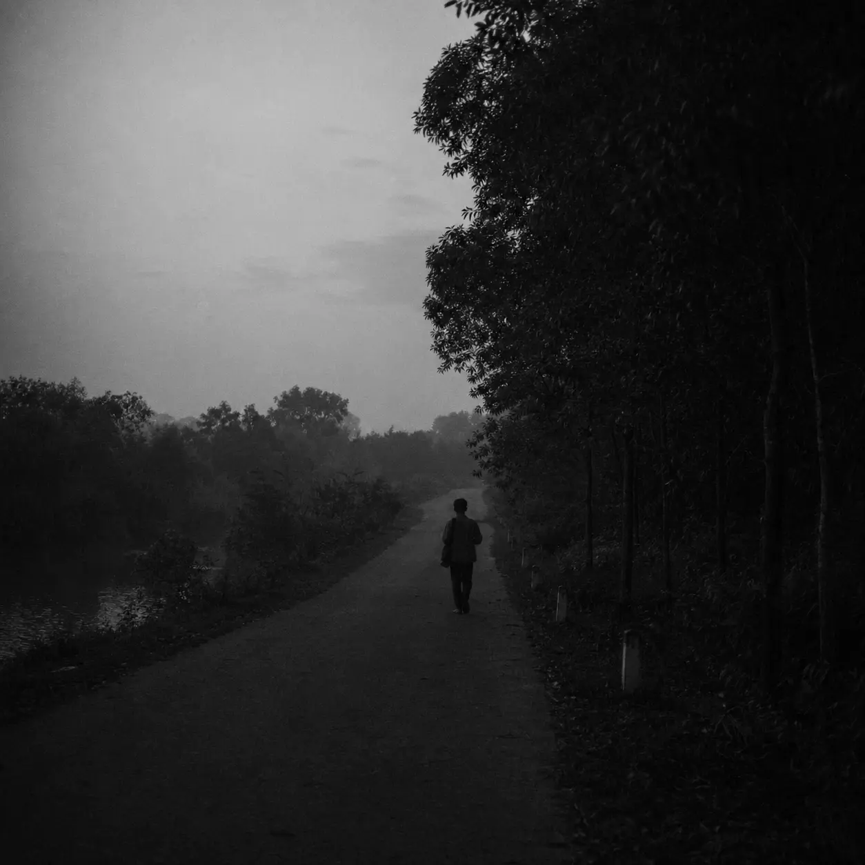 Black and white rural road scene with an anonymized adult young man walking away